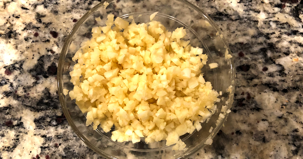 Minced garlic cloves in a clear glass bowl on counter.