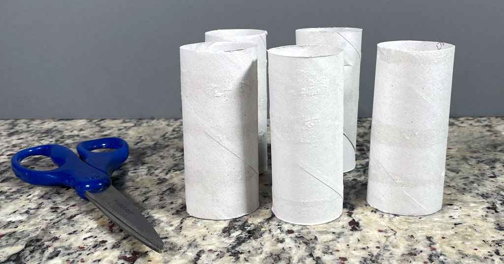 Five toilet paper rolls without toilet paper and a pair of scissors with blue handles