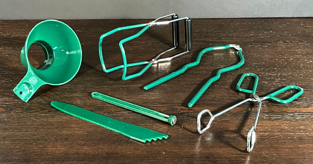 Set of green coated canning tools. Funnel, jar lifter, jar wrench, tongs, de-bubbler/headspace measurer, and magnetic lid lifter.
