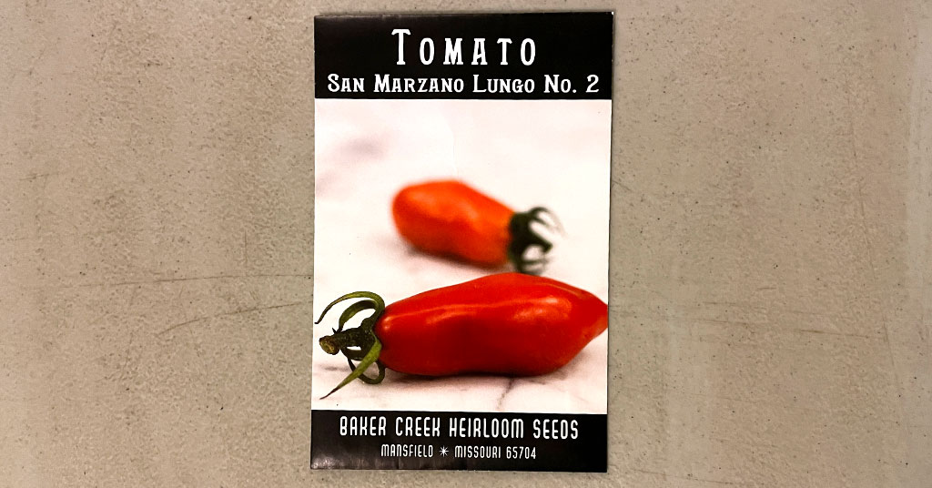 Front of a seed packet for San Marzano Lungo No. 2 tomatoes. Shows two tomatoes and the name of the company that packaged the seeds. Baker Creed Heirloom Seeds