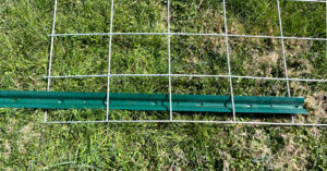 Green U-Post threaded through edge of cattle panel sitting on the grass.