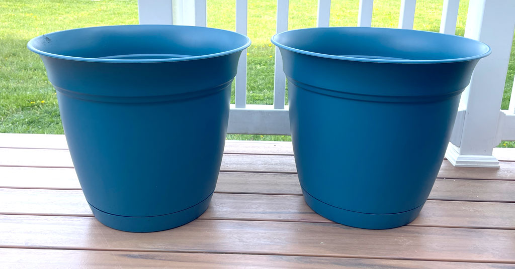 Two large blue garden pots sitting on a deck in front of green grass.