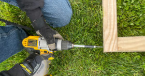 Screwgun being used to connect the corner of a raised garden bed with exterior wood screws.