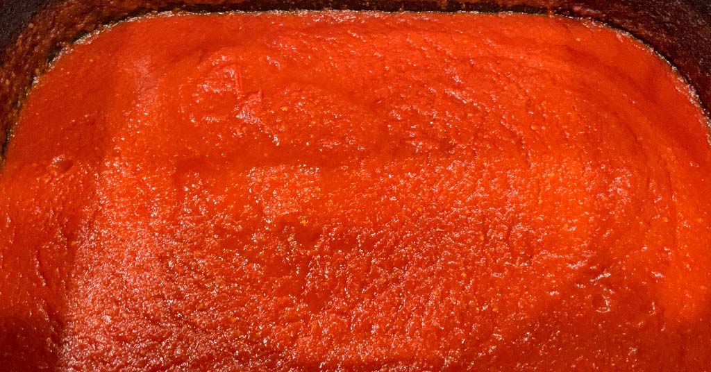 Red tomato sauce in an electric roaster. Sauce being reduced to a thicker sauce.