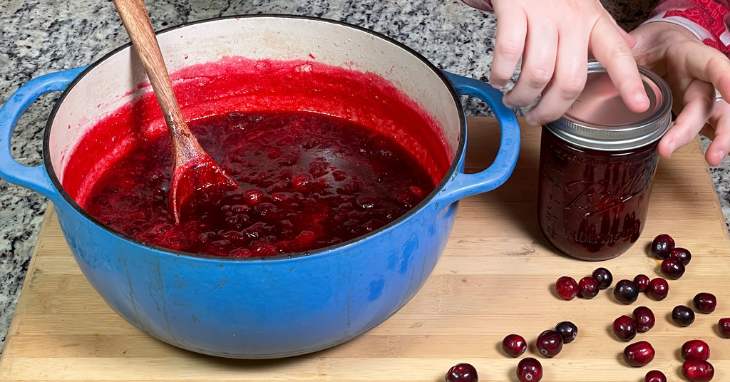 Cranberry Sauce in a blue enameled dutch oven. Pint Jar of cranberry sauce before water bath canning.