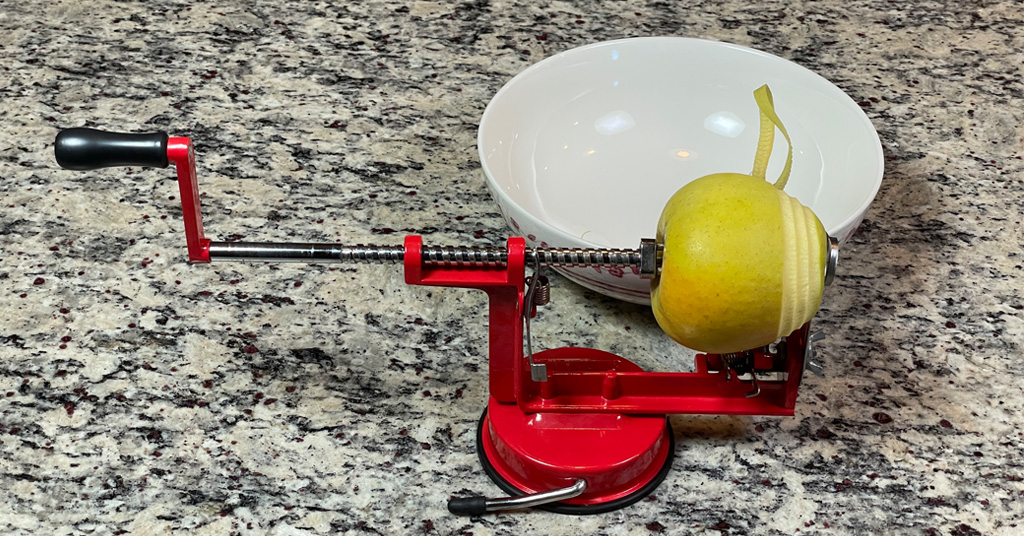 Red Apple peeler, corer, slicer peeling a yellow apple into a white bowl.