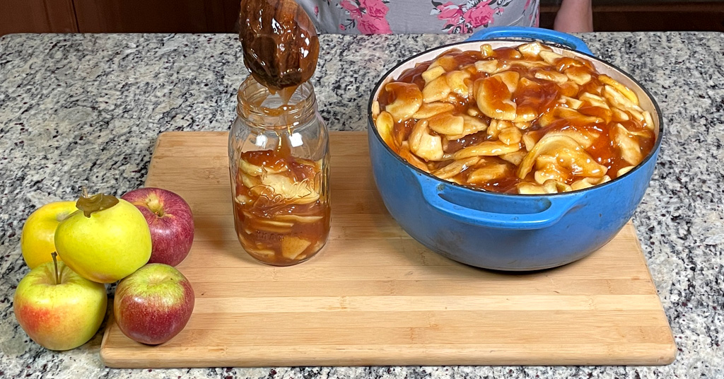 Apple pie filling in a blue enameled dutch oven. Apple Pie Filling is being ladled into Quart Size Canning Jars before water bath canning.