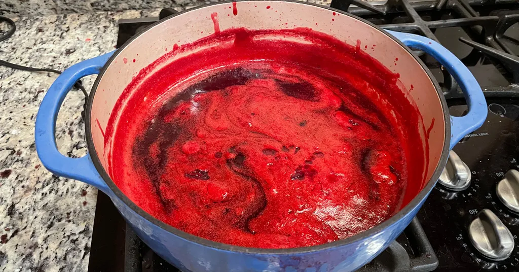 Cranberry Jelly before foam has been removed in a blue enameled dutch oven on stove.