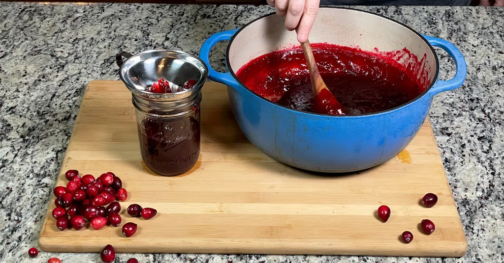 Ladling Hot Cranberry Jelly into Ball Pint Mason Jar using a funnel.