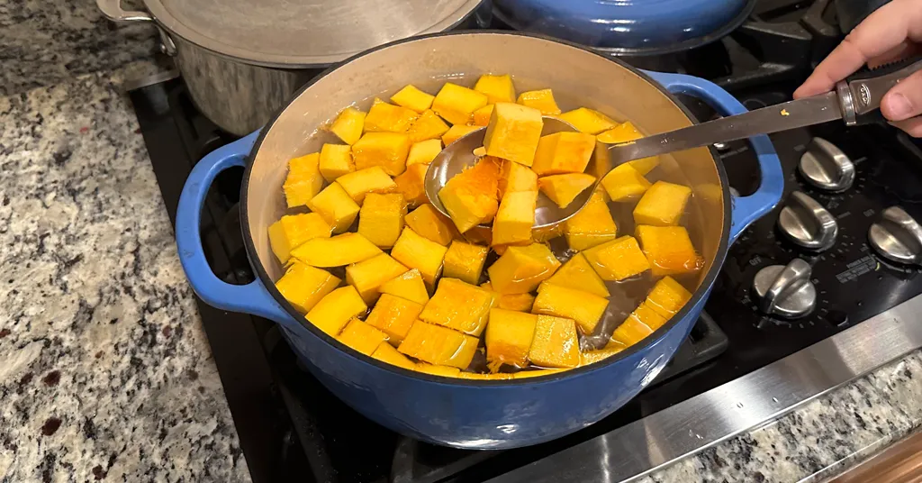 Pumpkin cubes being boiled in a blue enameled dutch oven.
