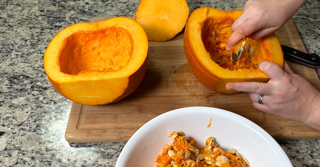 Pie Pumpkin cut in half. Hand removing seeds from the pumpkin halves with a spoon.