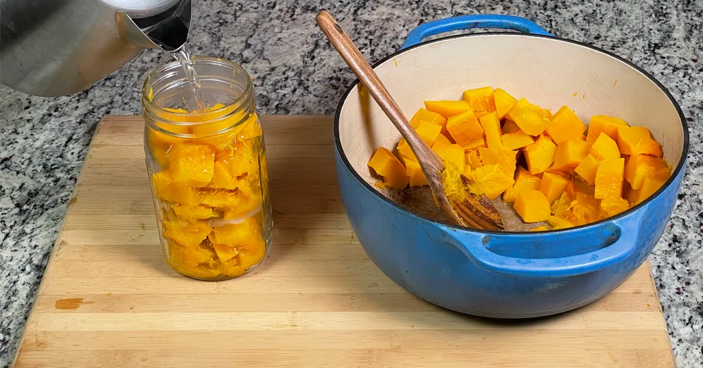 Boiling water from a tea kettle being poured on pumpkin cubes in a quart sized mason jar.