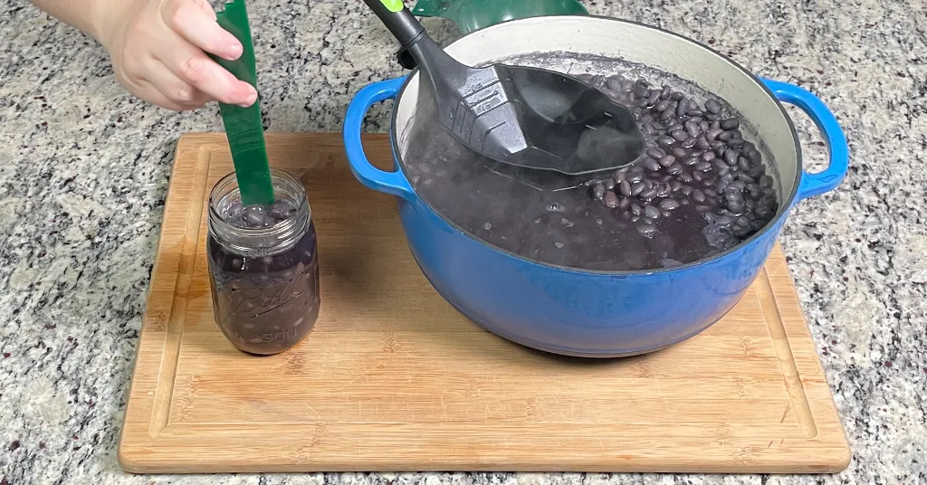 When Pressure Canning Dry Beans remove bubbles from your mason jar using a debubbler. Black Beans in a pint size mason jar next to a blue dutch oven full of black beans.
