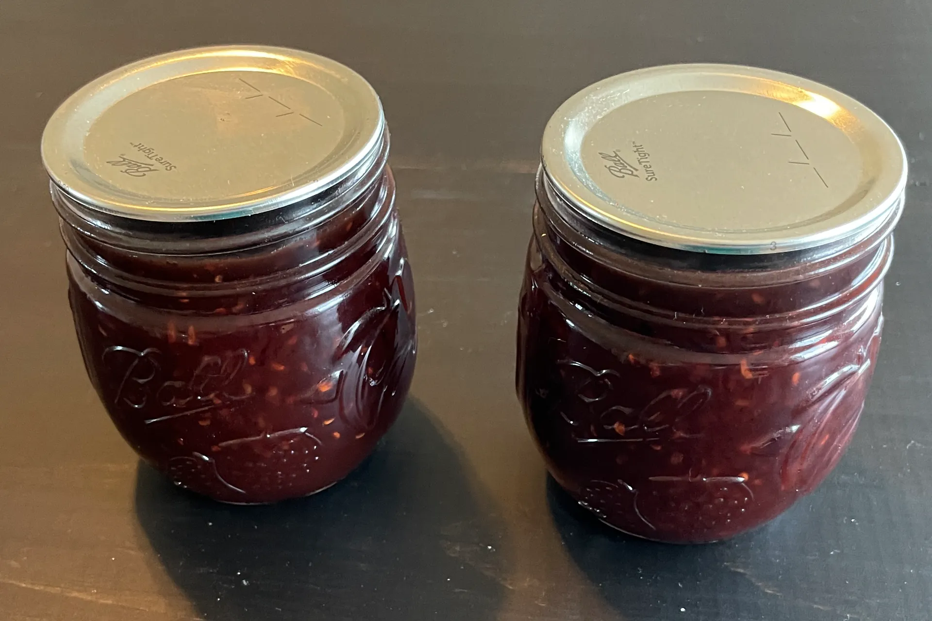 Two mason jars of Chocolate Raspberry Sauce that has been Water Bath Canned.