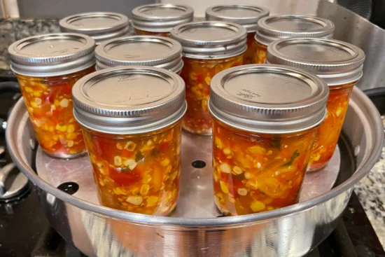 Half pint mason jars of corn and cherry tomato salsa from Ball Canning's recipe. Mason jars are sitting in the bottom of a steam canner.