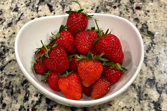 White bowl sitting on a counter full of delicious red ripe strawberries.