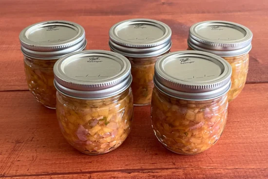 Five mason jars of peach salsa sitting on a wooden board.