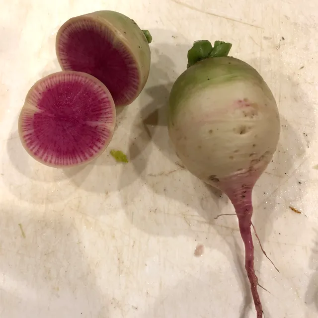 Two watermelon radishes sitting on a cutting board. One radish is cut open so you can see the pink inside.